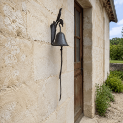 Petite cloche de porte oiseau en fonte sur une façade en pierre
