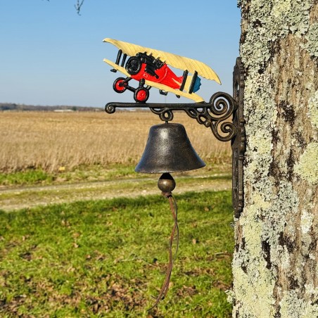 Cloche murale en fonte installée sur un mur avec un avion biplan coloré