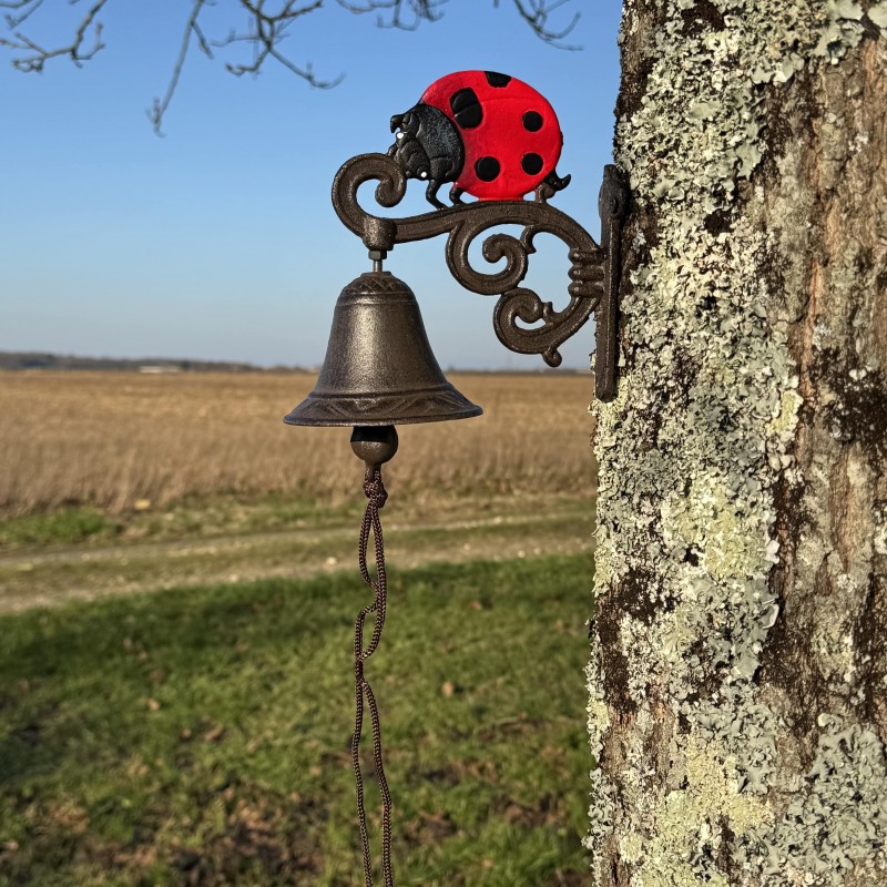 Cloche murale en fonte avec coccinelle installée dans un décor champêtre