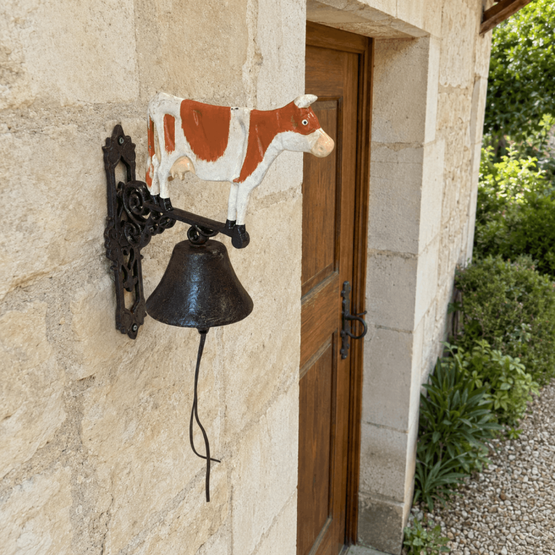 Grande cloche de porte vache en fonte sur façade en pierre